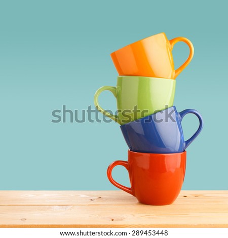 Pile of colorful cups on wooden table on blue background Royalty-Free Stock Photo #289453448