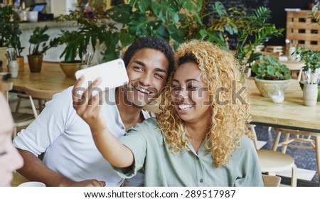 Attractive friends taking self portrait photograph selfie in cafe