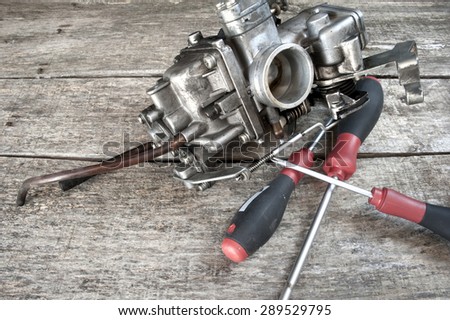 Carburetor and screwdrivers on wooden surface