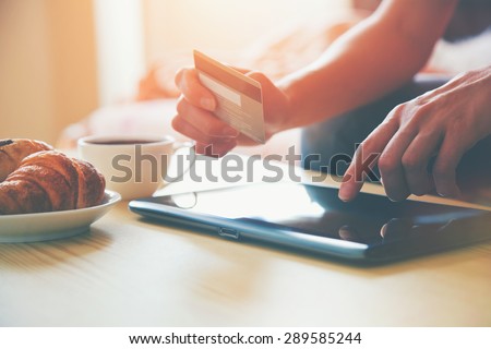 Hands holding credit card and using digital tablet pc with morning coffee and croissant. Online shopping. Royalty-Free Stock Photo #289585244
