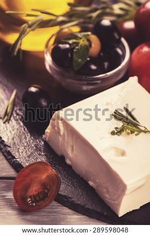 Greek feta cheese with fresh herbs, black and green olives, cherry tomatoes, selective focus. Toned image
