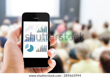 Close-up hand holding mobile phone with analyzing graph against people in business conference and presentation background  Royalty-Free Stock Photo #289663994