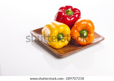 Three colorful fresh red, orange, yellow sweet pepper(pimenta, bell pepper, pimento) on the wood dish(tray, bowl) isolated white at the studio.