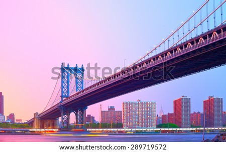 Manhattan bridge in New York CIty USA on a beautiful colorful summer sunset with illuminated downtown buildings and moving traffic