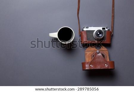 White cup of coffee and retro camera in leather case on grey background