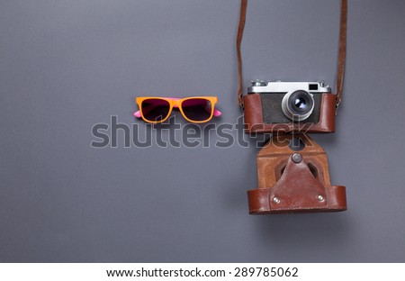 orange glasses and retro camera in leather case lying down on grey background