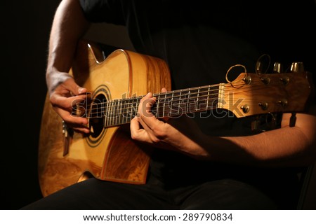 Young man playing on acoustic guitar on dark background Royalty-Free Stock Photo #289790834