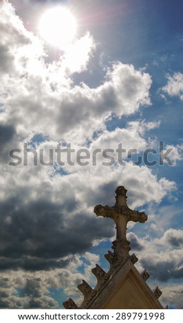 Old gravestone cross at French cemetery and sun rays glow through the clouds. 
