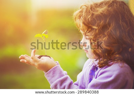Little girl holding young plant in spring outdoors. Ecology concept. Background toning to instagram filter.