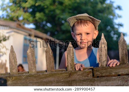 Portrait of a Cute Young Boy with Cowboy Hat Holding at the Wooden Fence, Smiling at the Camera