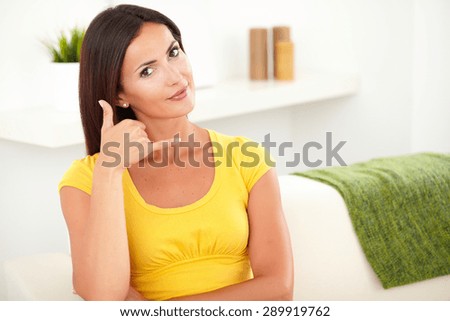 Caucasian woman making a call me sign while sitting on the couch indoors