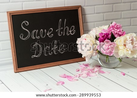 Beautiful bouquet of pink and white peonies in the glass vase with petals on the light grey brick and wood background.