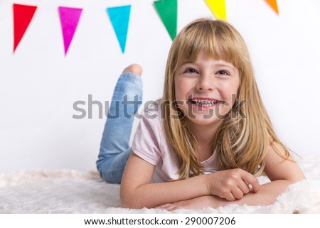 child blonde happy girl in pink shirt over white background lying on the floor