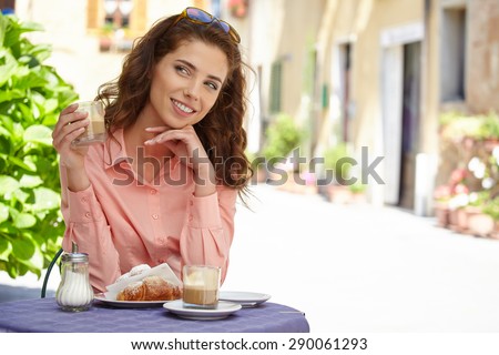 Portrait of beautiful blond woman sitting in outdoors cafe in Italy, drinking coffee and eating croissant.