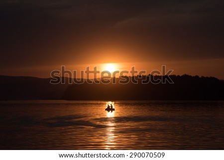 Silhouette of fisher and dog sitting in boat