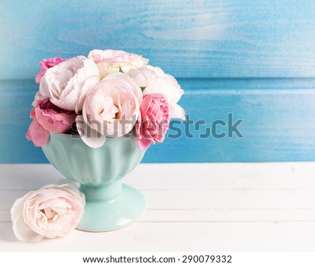 Pastel roses in turquoise vase on white wooden  background against blue wall. Place for text. Selective focus. Toned image.
