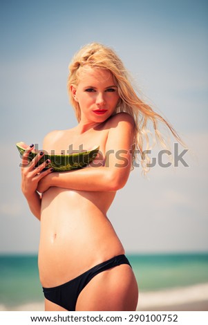 young beautiful slender girl , attractive blonde, enjoys tropical hot weather, eats  fresh, aromatic a water-melon, wind develops beautiful long hair
