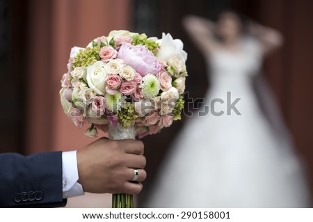 Groom holding beautiful fresh wedding bunch of pink lilac purple white and violet chrysanthemum rose and peony flowers in hand closeup on blur bride background, horizontal picture