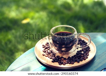 Hot black coffee on wooden table green grass background