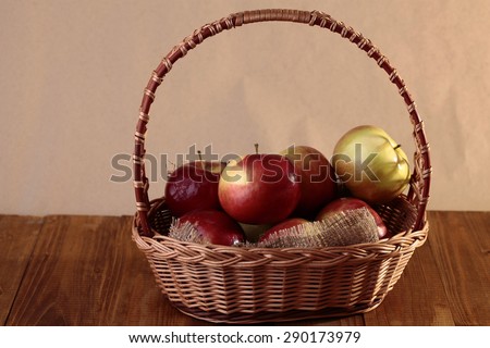 Full wicker basket with fresh juicy red and green apples on wooden table top on light brown background, horizontal picture