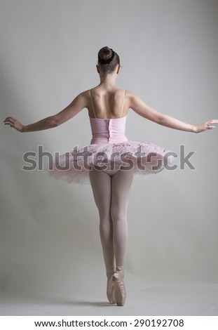 Young ballerina in a pink ballet tutu is dancing on a white background
