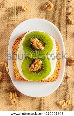 Toast with kiwi, cheese and walnuts on a piece of sackcloth with walnuts around. View from above  Royalty-Free Stock Photo #290221643