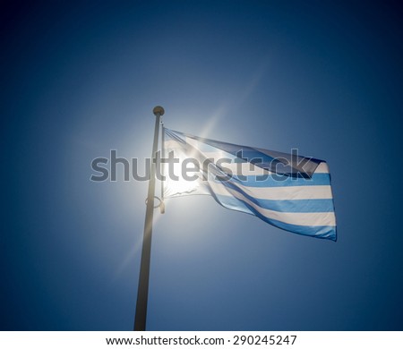 Greek flag waving before sun on blue sky, contre-jour backlighting
