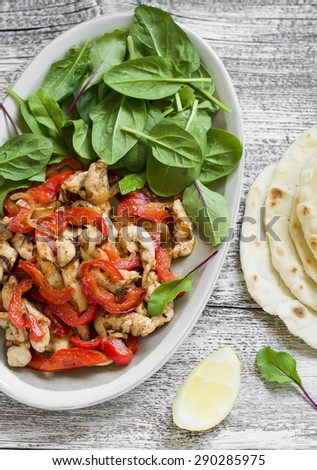 stir fry of chicken breast and sweet red peppers, fresh spinach and homemade tortillas on a light wooden background