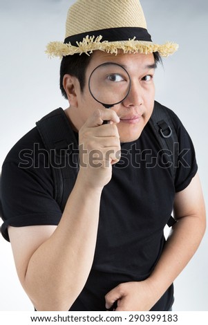 portrait of a young asian man looking through a magnifying glass on gray background