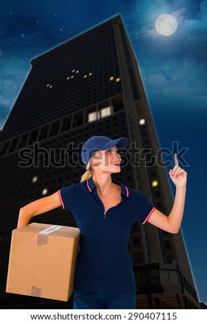 Happy delivery woman holding cardboard box and pointing up against city at night