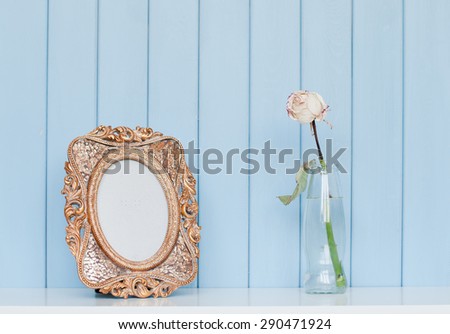 Old vintage picture frame and rose in the bottle on blue wooden background