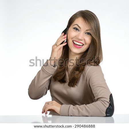 Portrait of a sweet young woman who is talking on the phone and sitting at a table in a brown dress, photo on the white background.