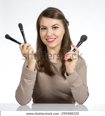Portrait of a sweet young woman holding a cosmetic brush and sits at a table in a brown dress, photo on the white background.