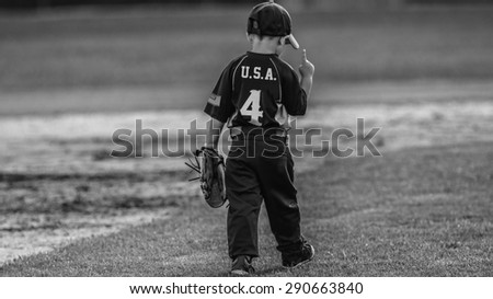 Team USA
Picture of a young boy walking away from the camera. He's wearing  a baseball uniform with U.S.A. on the back and an American flag on his sleeve. He's holding 1 finger in the air.