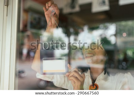 Smiling woman hanging open sign on the glass door