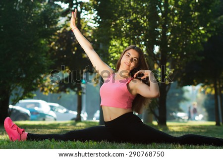 Pretty sportswoman doing exercises in outdoor park setting, green trees background