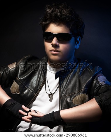 Portrait of happy young stylish biker over dark blue background, wearing fashionable sunglasses and leather jacket, fashion for motorcyclists
