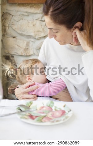 blonde two years age baby with pigtails breastfeeding woman mother white jersey sitting in restaurant table