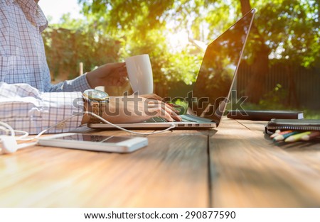 Escaped of office.
Business style dressed man sitting at natural country style wooden desk with electronic gadgets around working on laptop drinking coffee sunlight and green terrace on background Royalty-Free Stock Photo #290877590