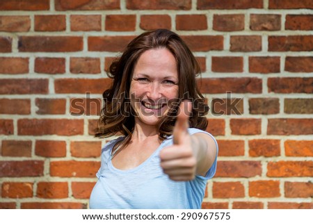 Woman shows a thumbs up, in the background is a brick wall