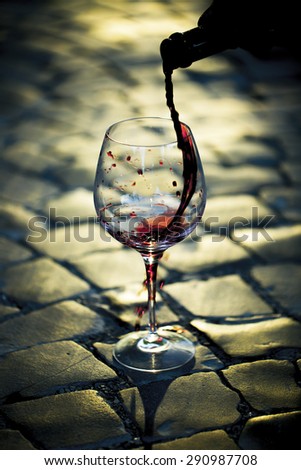Red wine poured in bocal standing on block stone road in daylight on outdoor sepia background, vertical picture