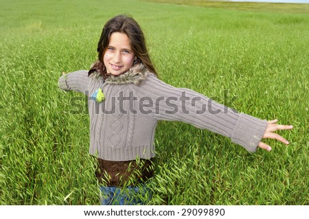 Beautiful young girl in a windy green field with open arms