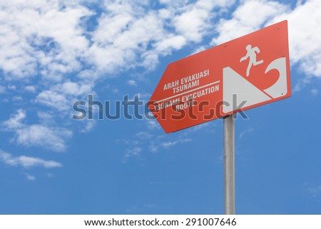 Tsunami warning orange sign "Evacuation route " with picture of waves and escaping man figure standing on the ocean coast against blue sky background
