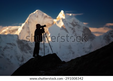 A silhouette of a man (photographer) standing on a hills in front of the mountains. 