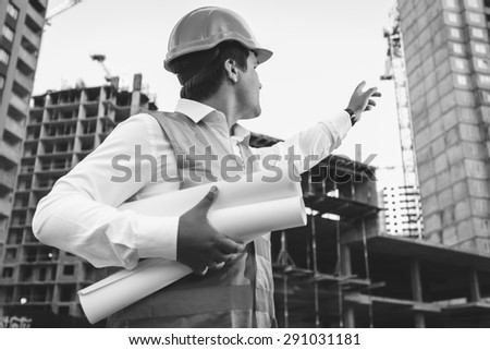 Black and white closeup photo of engineer with blueprints checking building site construction