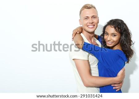 Sweet embrace. Portrait of a blond young man standing smiling embracing his beautiful girlfriend wearing blue shirt, isolated on white background