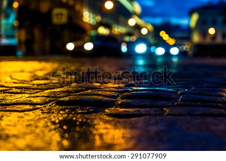 The bright lights of the evening city after rain, headlights from cars in the distance. View from the pavement level