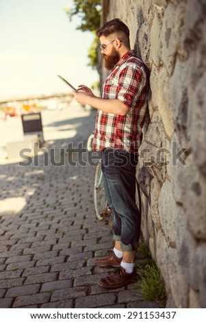 Trendy hipster young man using tablet. Posing next to stone wall