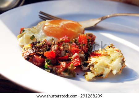 Traditional healthy breakfast on a white plate. It includes fried ham and eggs, tomatoes, pepper and onion. Only middle part of picture is in focus. The fork is on the background. 