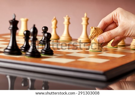 Playing chess - a male hand moving white chess knight on a traditional wooden chessboard